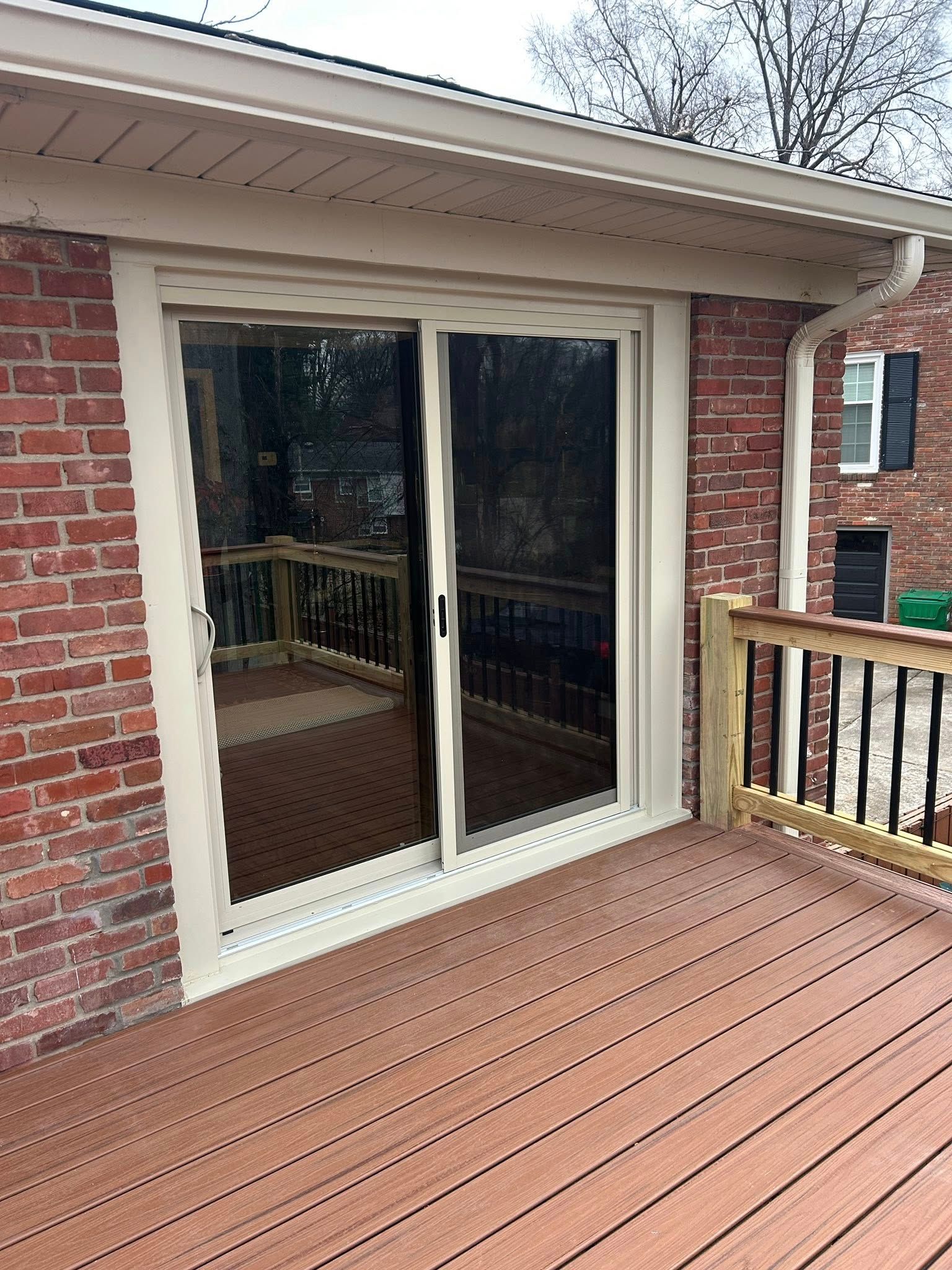 Sliding glass door on brick building opens to a wooden deck with railing.