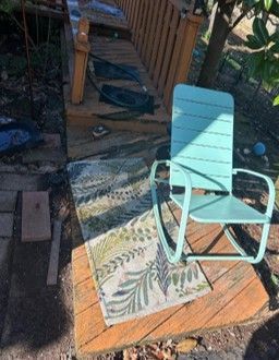 Mint-green rocking chair on a wooden deck with a patterned outdoor rug in sunlight. Mint-green rocking chair on a wooden deck with a patterned outdoor rug in sunlight.
