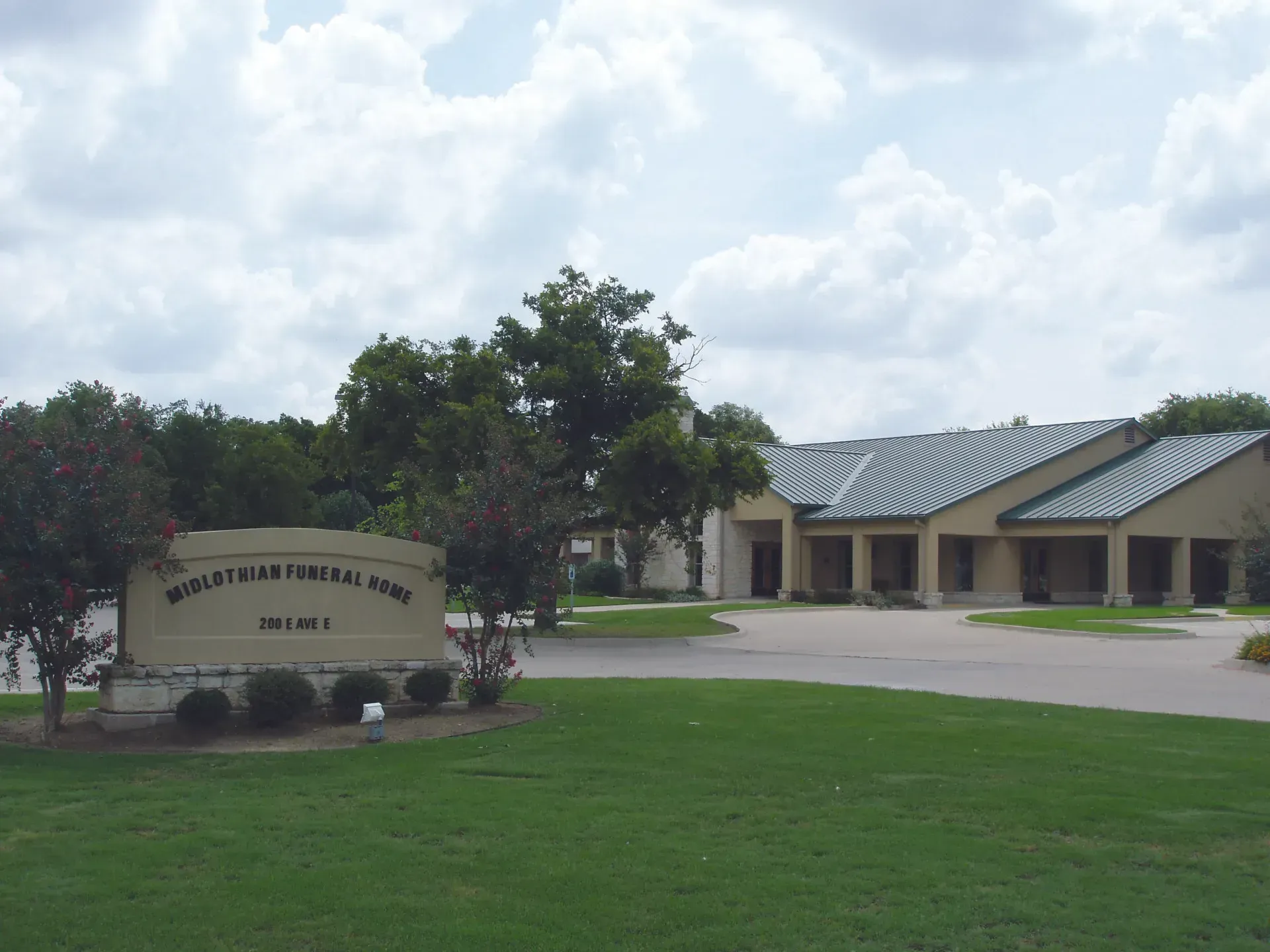 Elementary school building with a sign, green lawn, trees, and cloudy sky