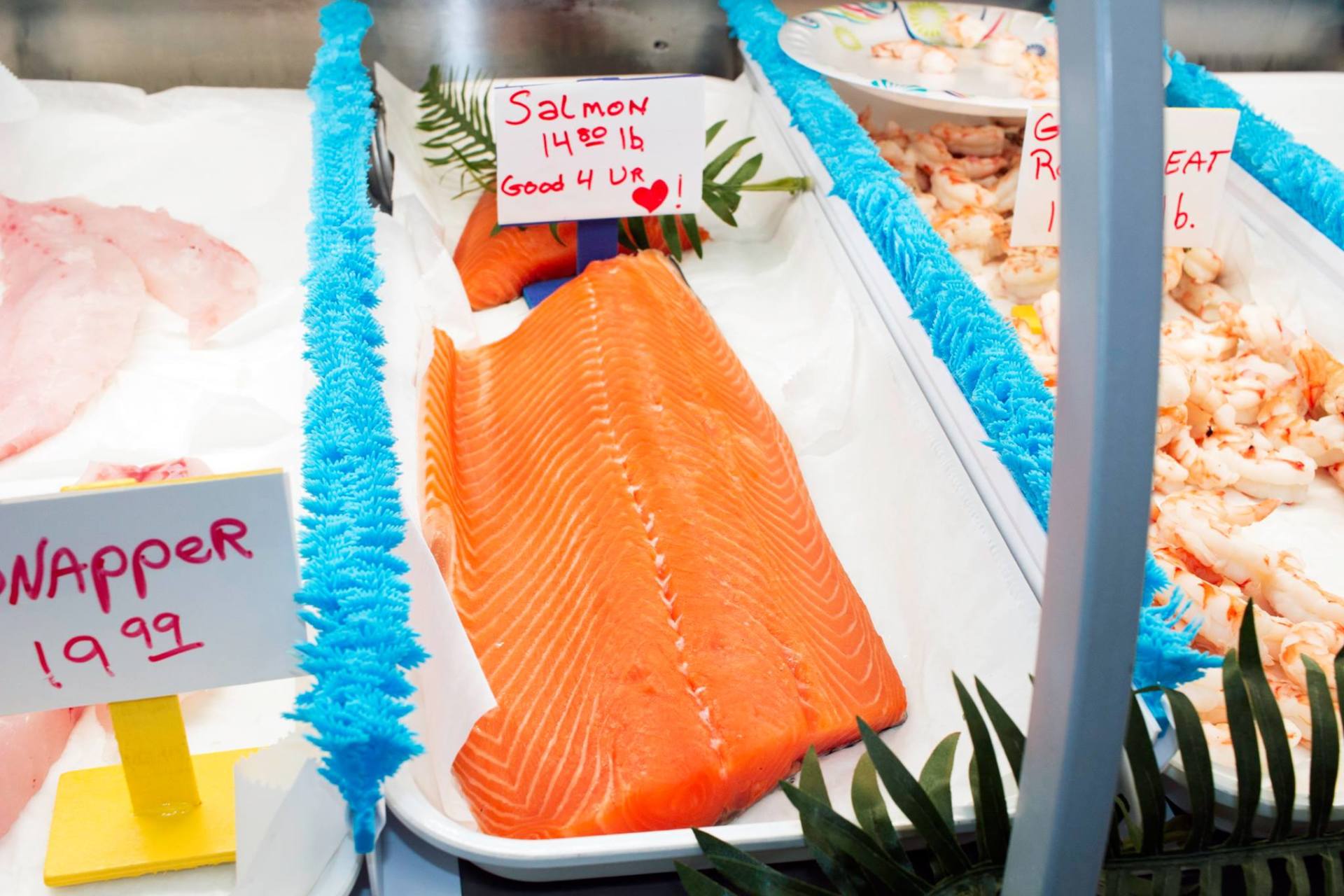 Fresh salmon fillet displayed in a seafood case with other fish and pricing signs.