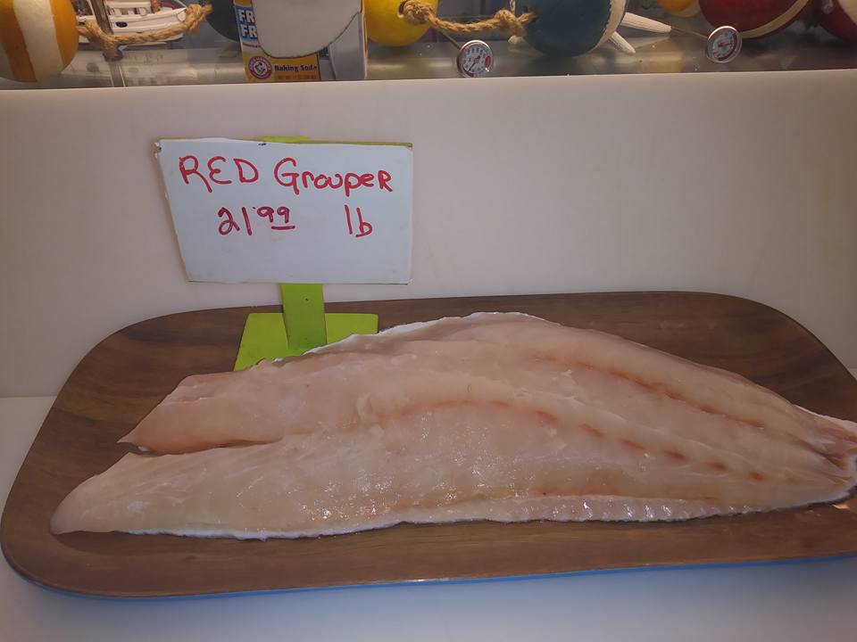 Red grouper fillets on a wooden tray with a price sign.