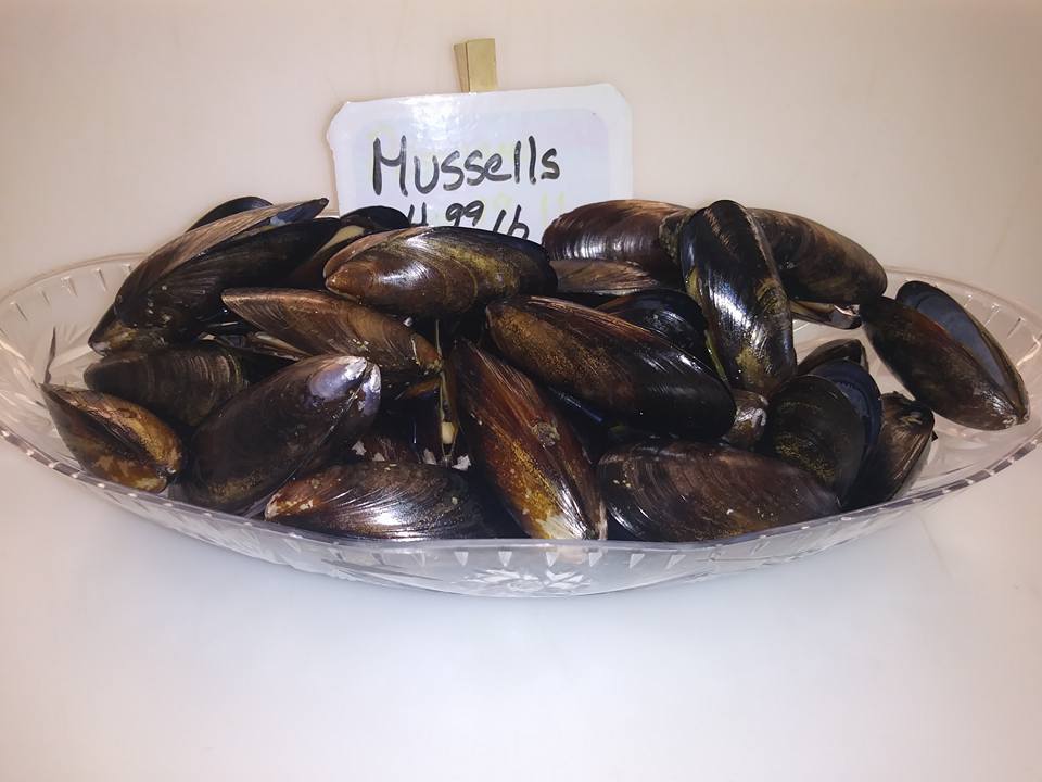 A clear glass dish overflowing with dark blue mussels, a price tag reads