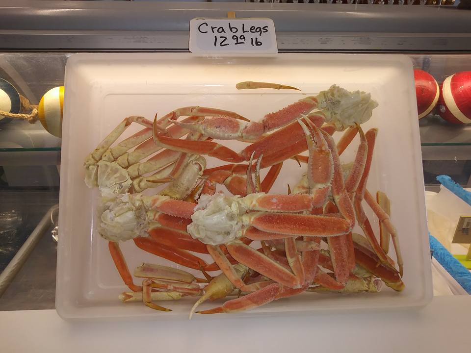 Crab legs in a plastic container, priced at $12/lb, displayed in a store setting.