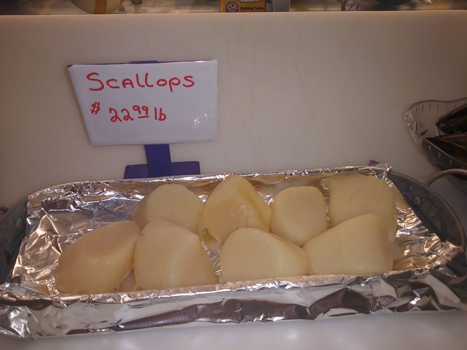 Scallops displayed in a tray lined with foil, price tag above them says $22.99/lb.