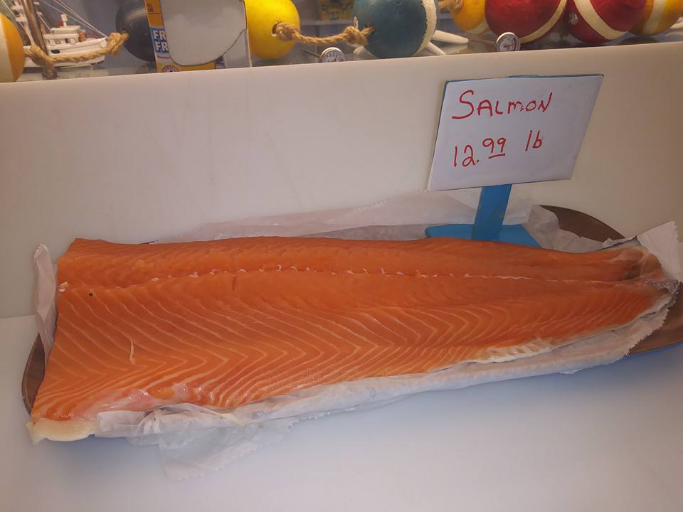 A large, raw salmon fillet in a display case with a 