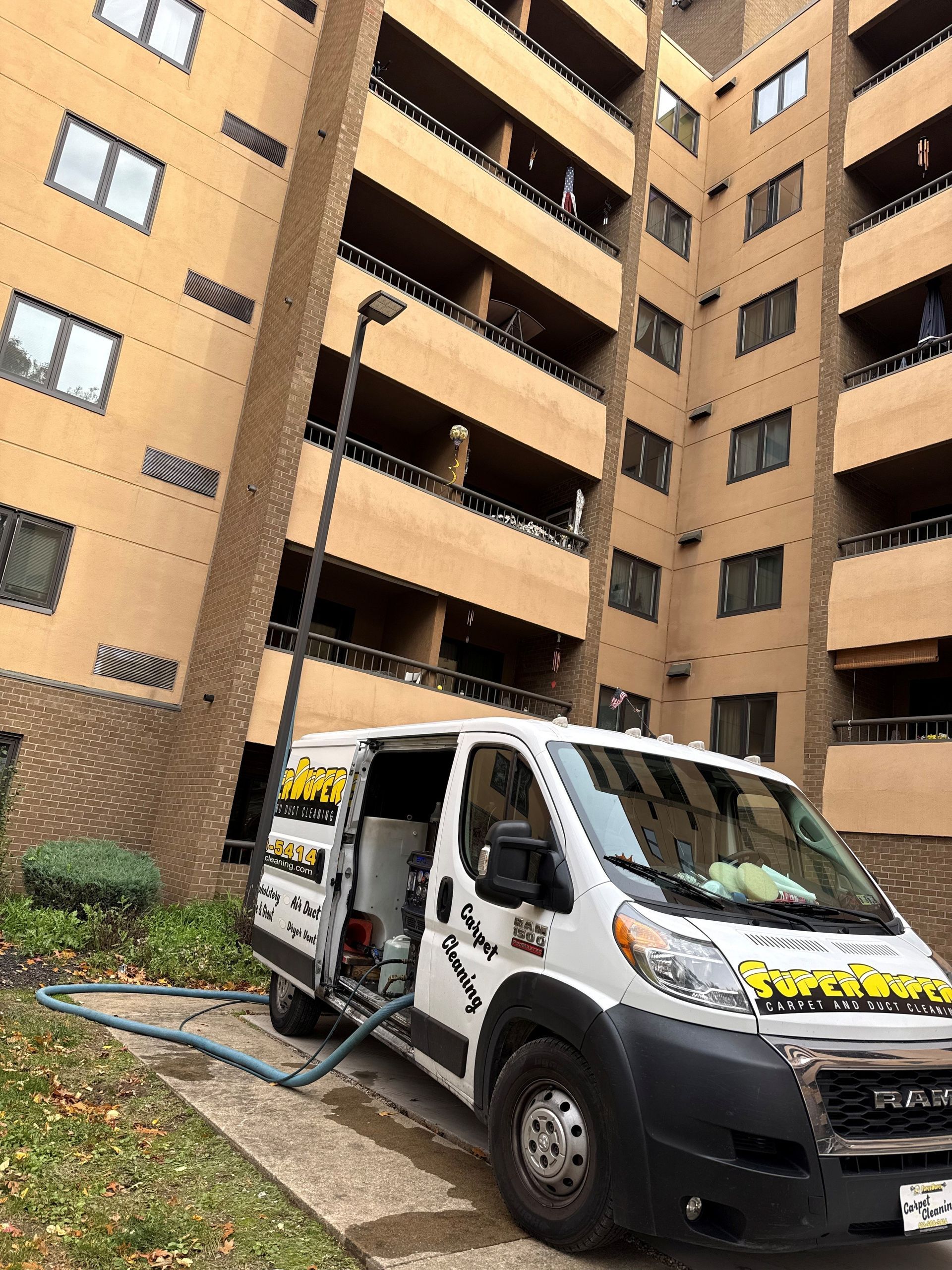 White van with opened door, hose, and tall building. 