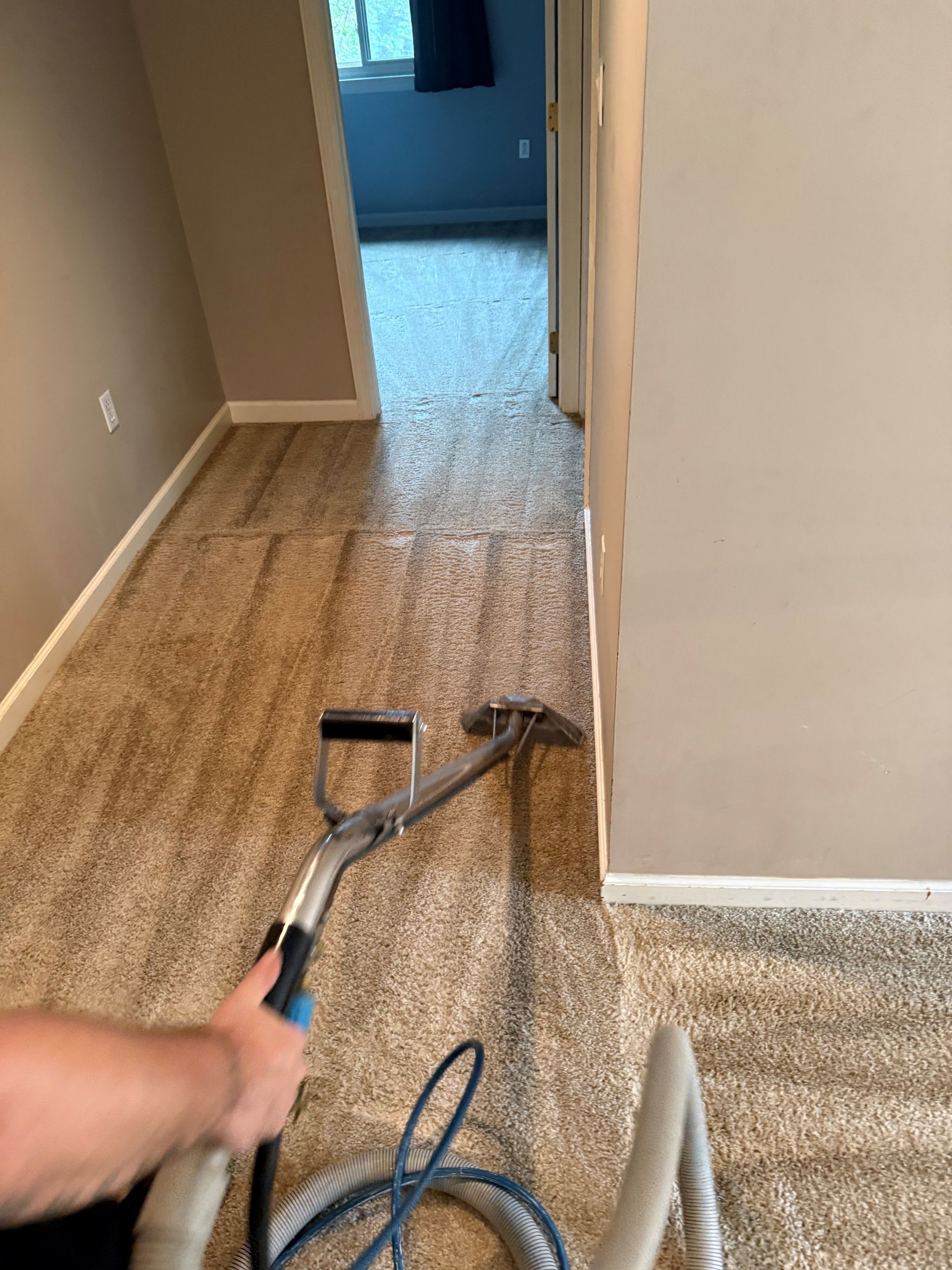 Person cleaning a carpeted hallway with a cleaning machine; beige carpet and walls.