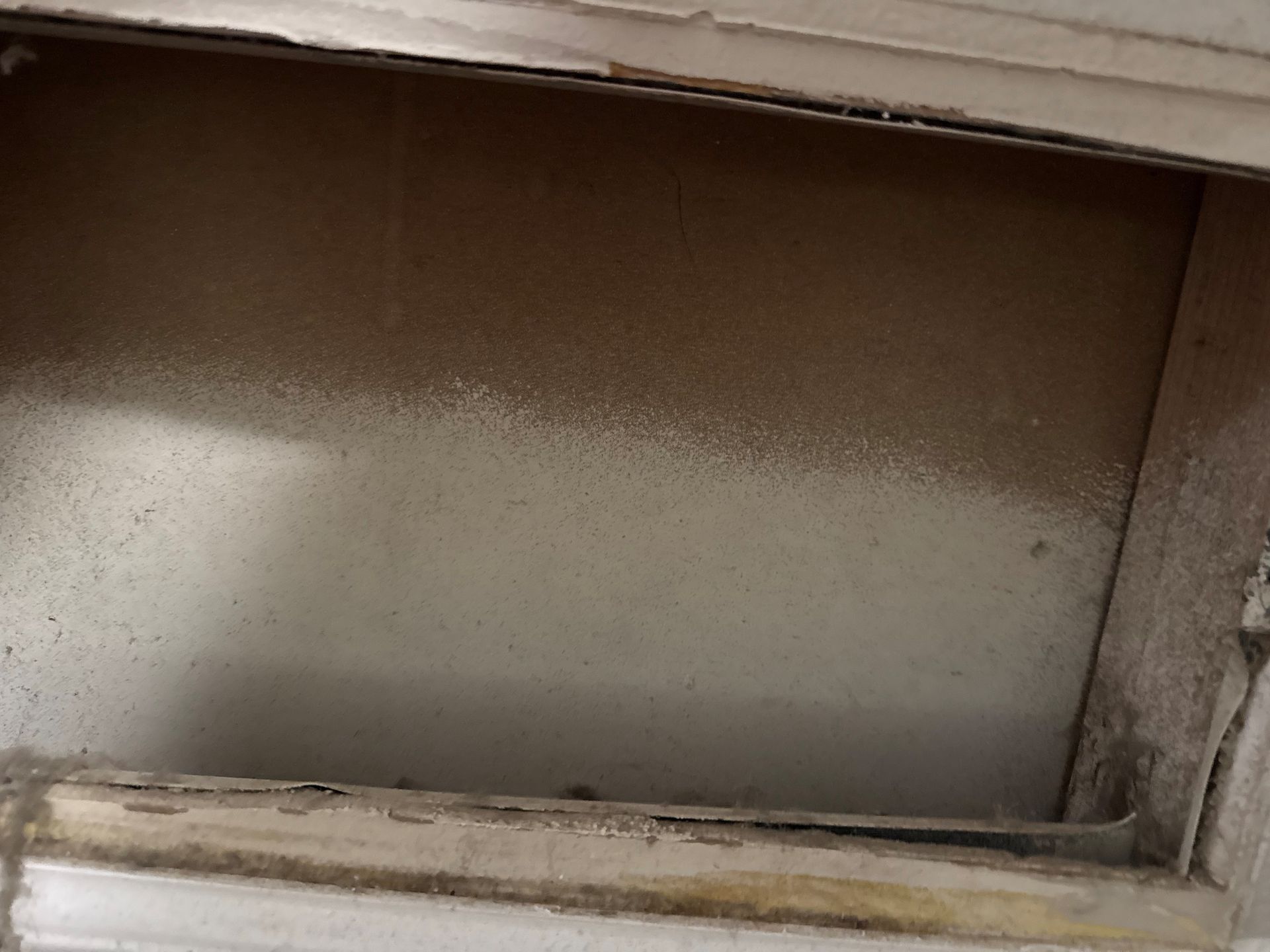 Dust-covered, recessed compartment with wooden trim, partially illuminated.