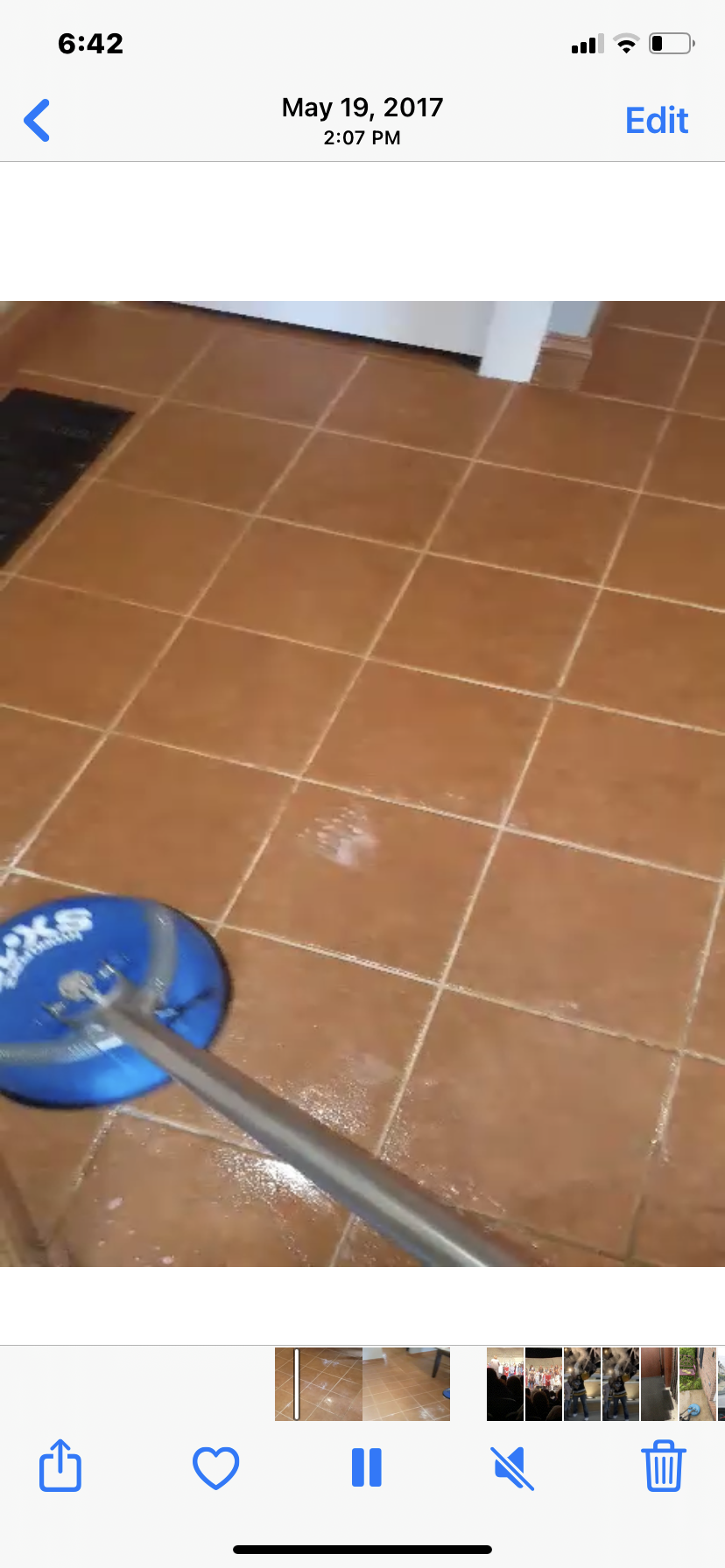 A person cleaning brown tile floor with a blue and silver cleaning tool.