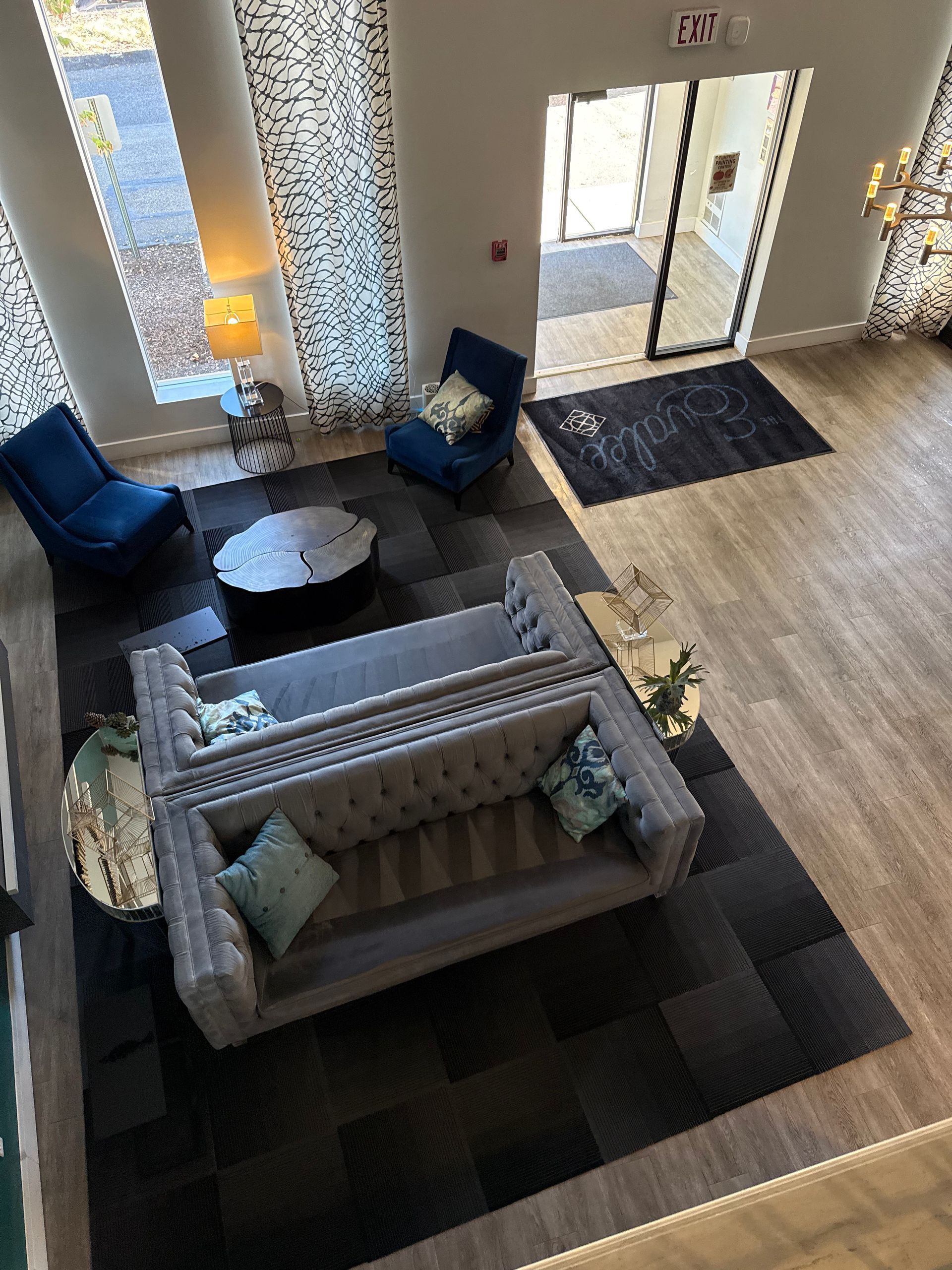 Lobby with gray sofa, blue chairs, black rug, and a door to the outside.
