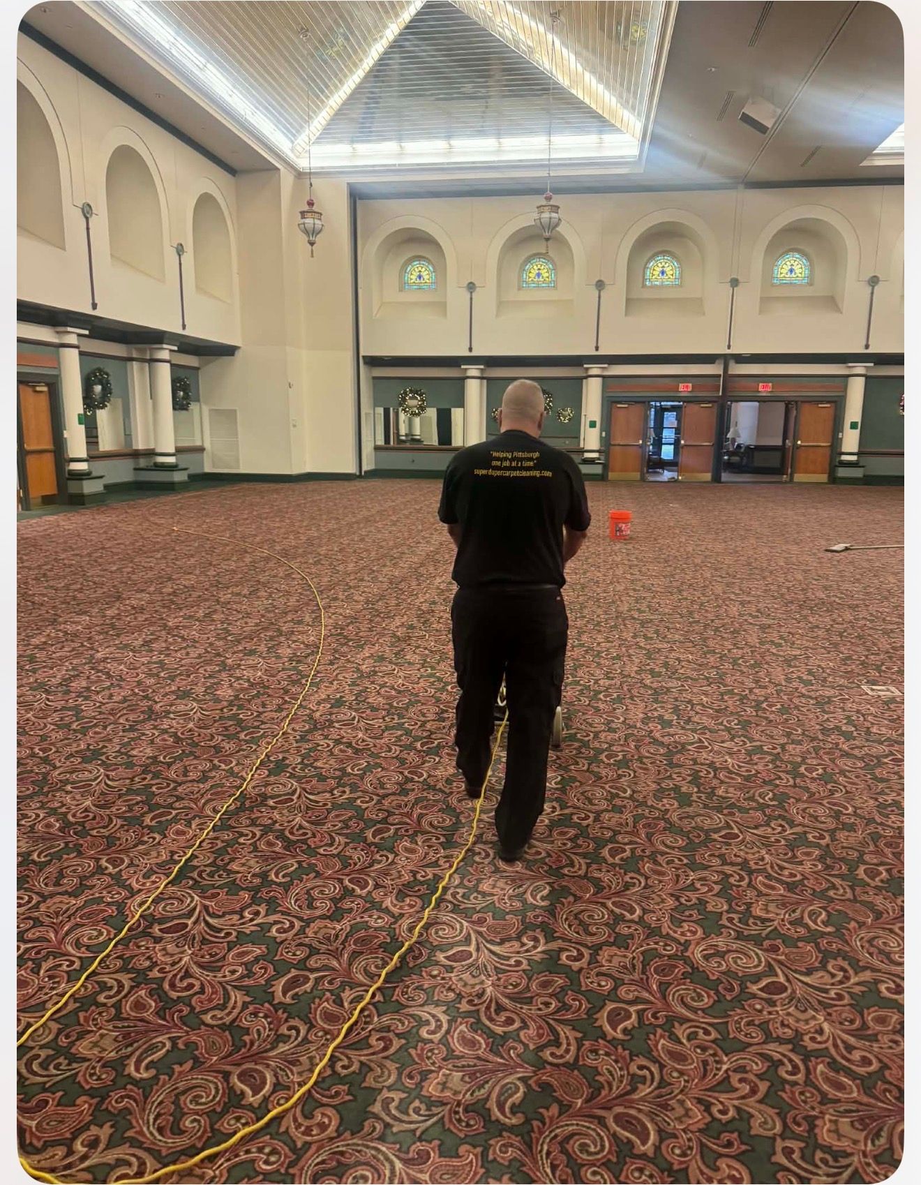 Person in black uniform walking across a large room with patterned carpet, holding a yellow cord.