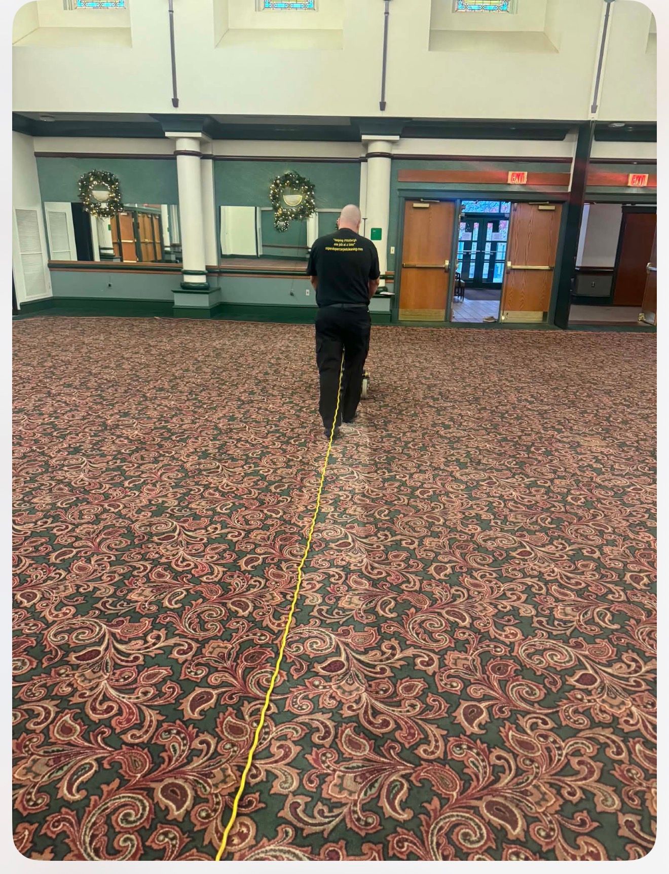 Man vacuuming patterned carpet in a large room.