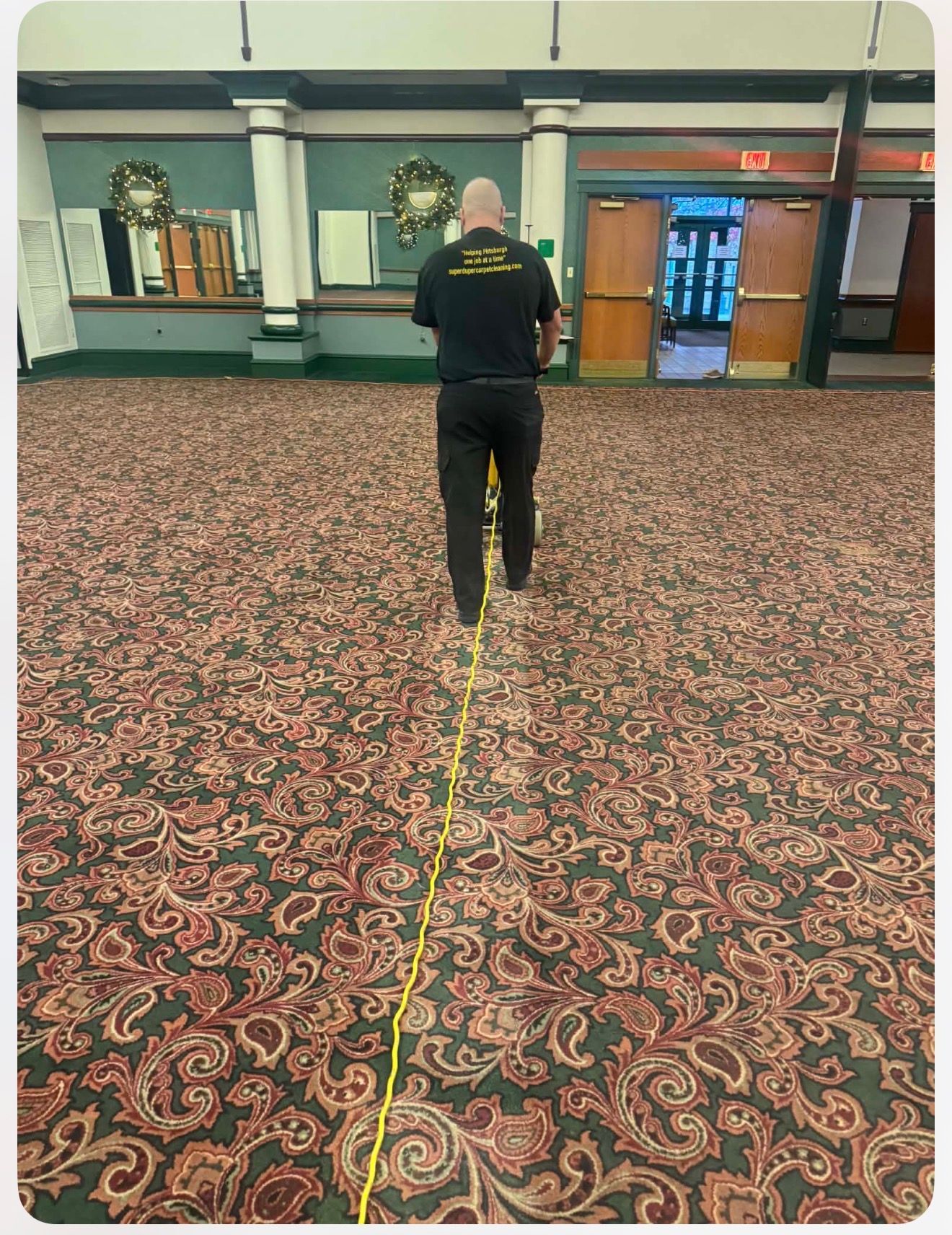 Person using a carpet cleaner in a large room with patterned carpet and columns.