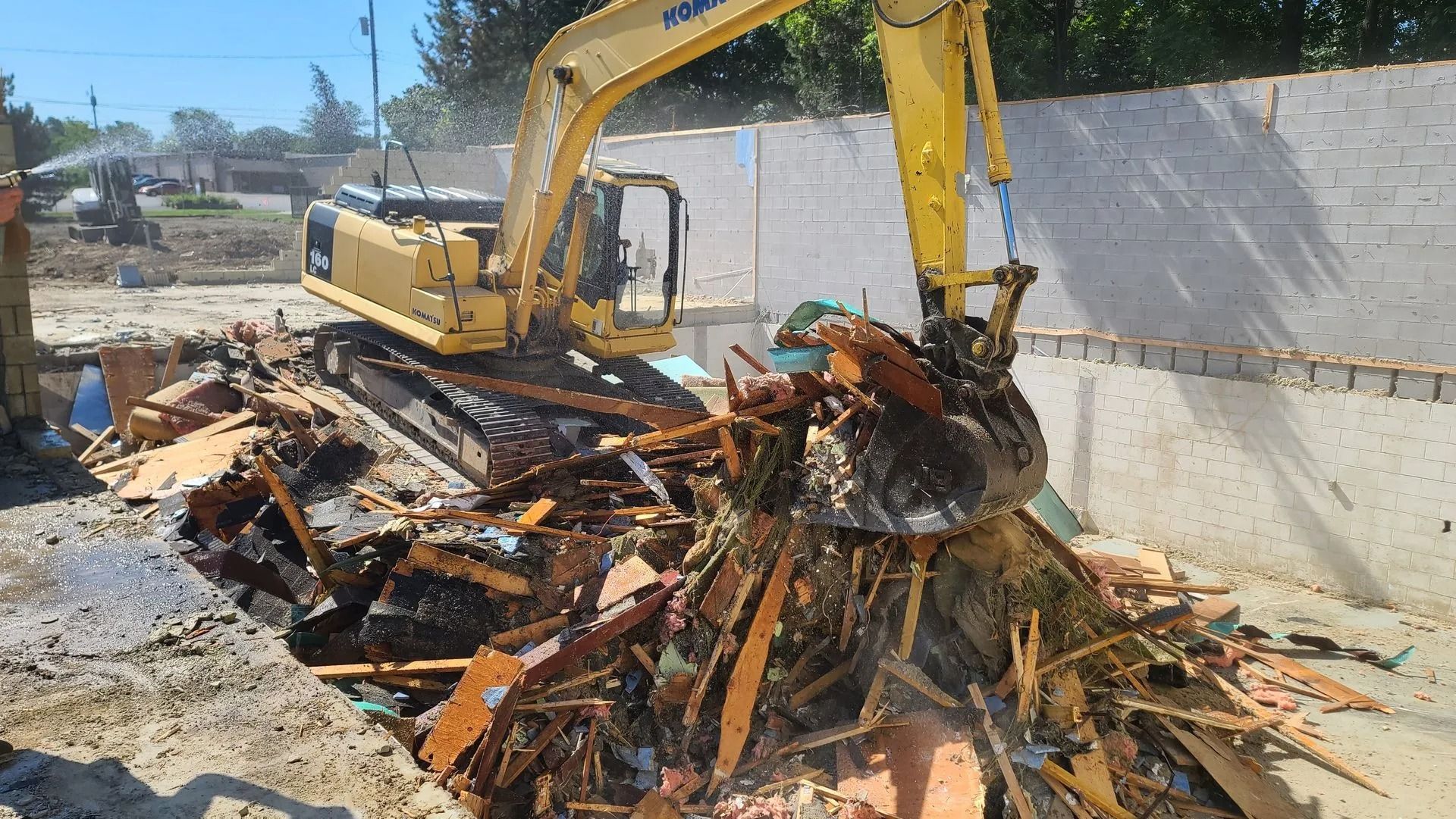 Yellow excavator demolishing a building, scooping debris.