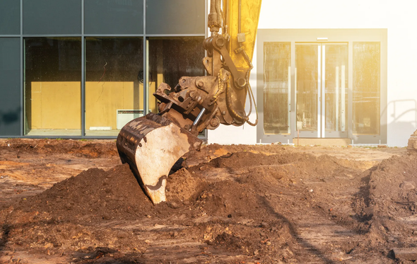 A bulldozer is digging a hole in the ground in front of a building.