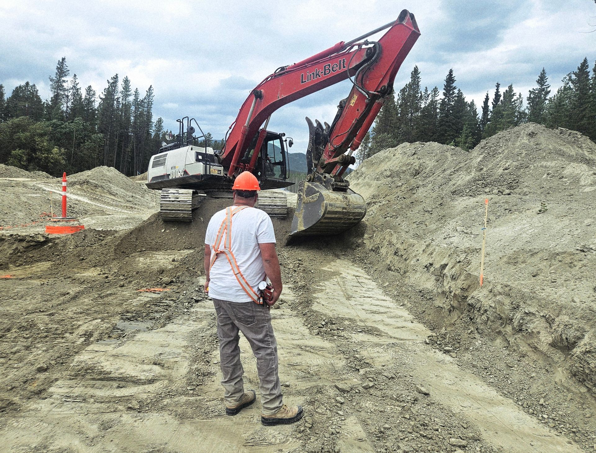 Man in safety gear watches excavator in construction site.