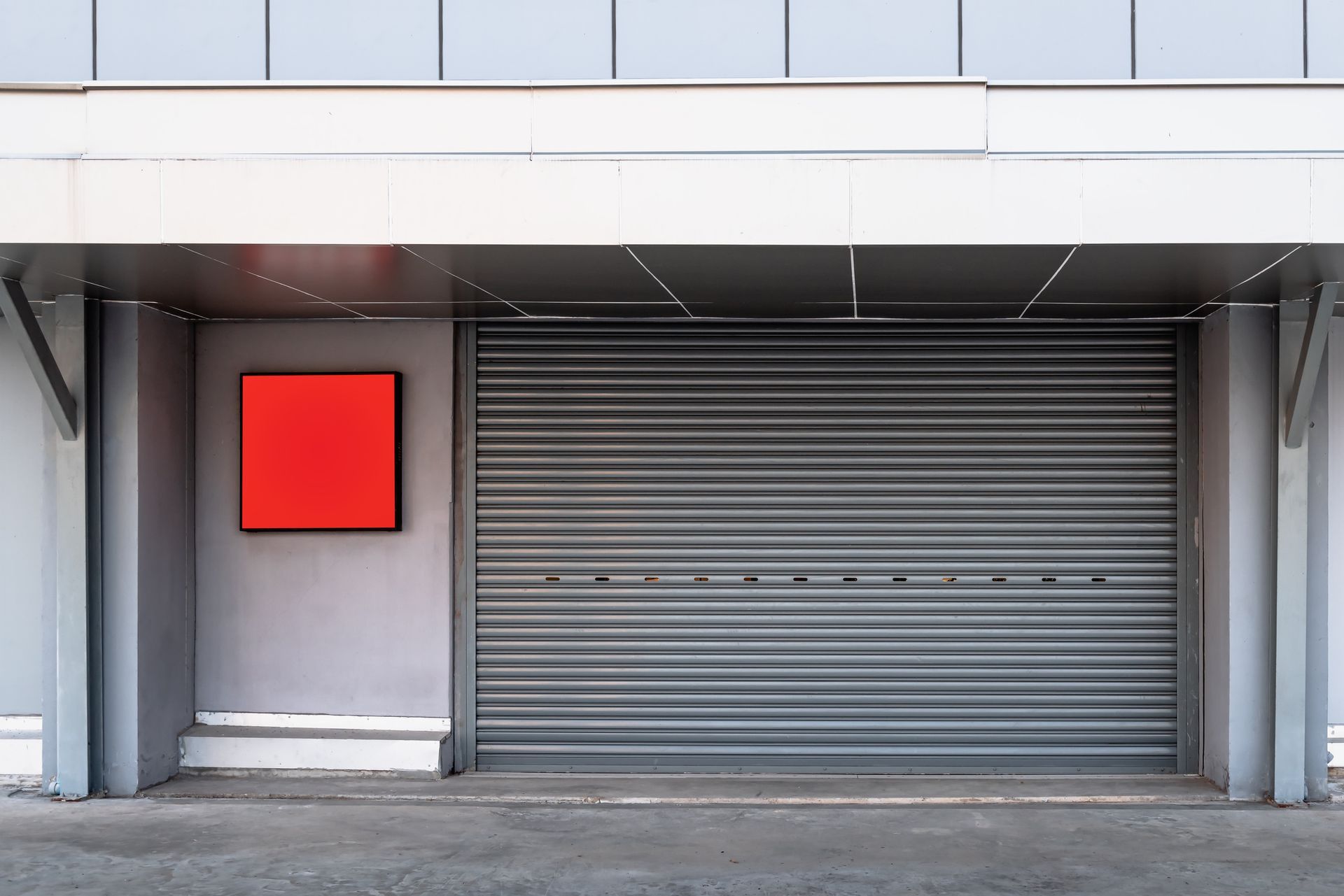 There is a red sign on the wall next to a garage door.