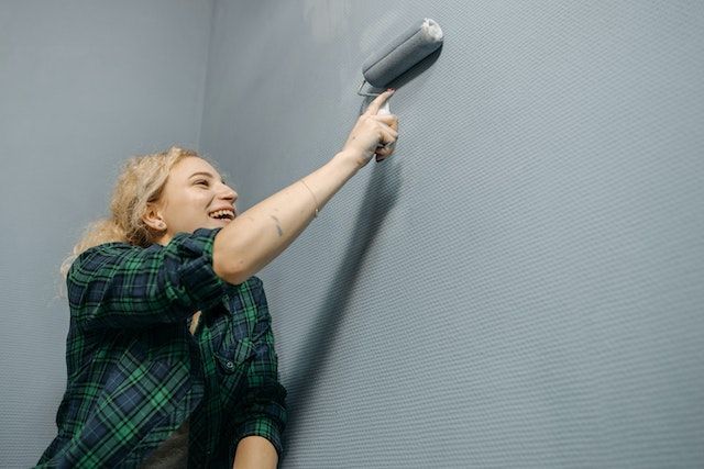 Person in  a green plaid shirt painting a wall blue-ish grey