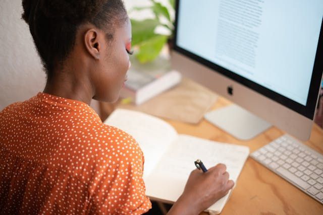 Person looking at computer and writing in a book