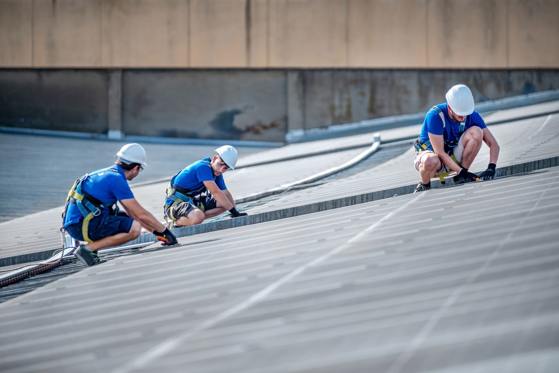 Three roofing contractors in safety gear working on a sloped roof.