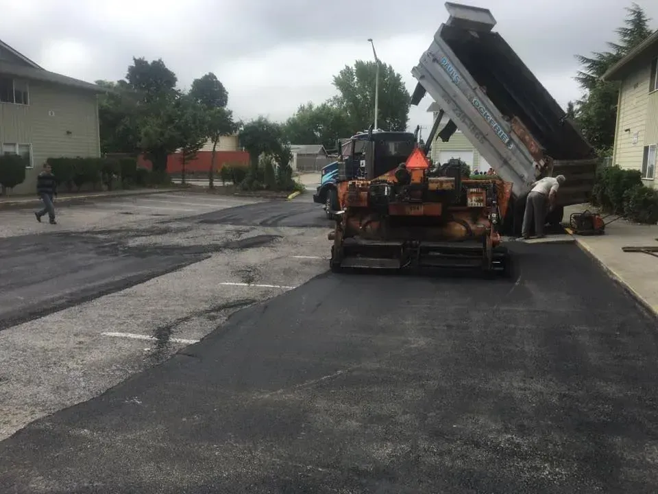 Asphalt paving in progress: truck dumping asphalt into a paving machine on a parking lot.