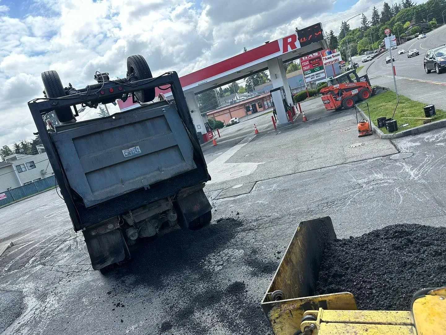 Dump truck unloading asphalt on a road near a gas station.