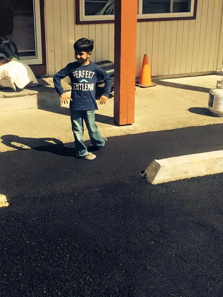 Boy in blue shirt and jeans standing on fresh asphalt, hands on hips.