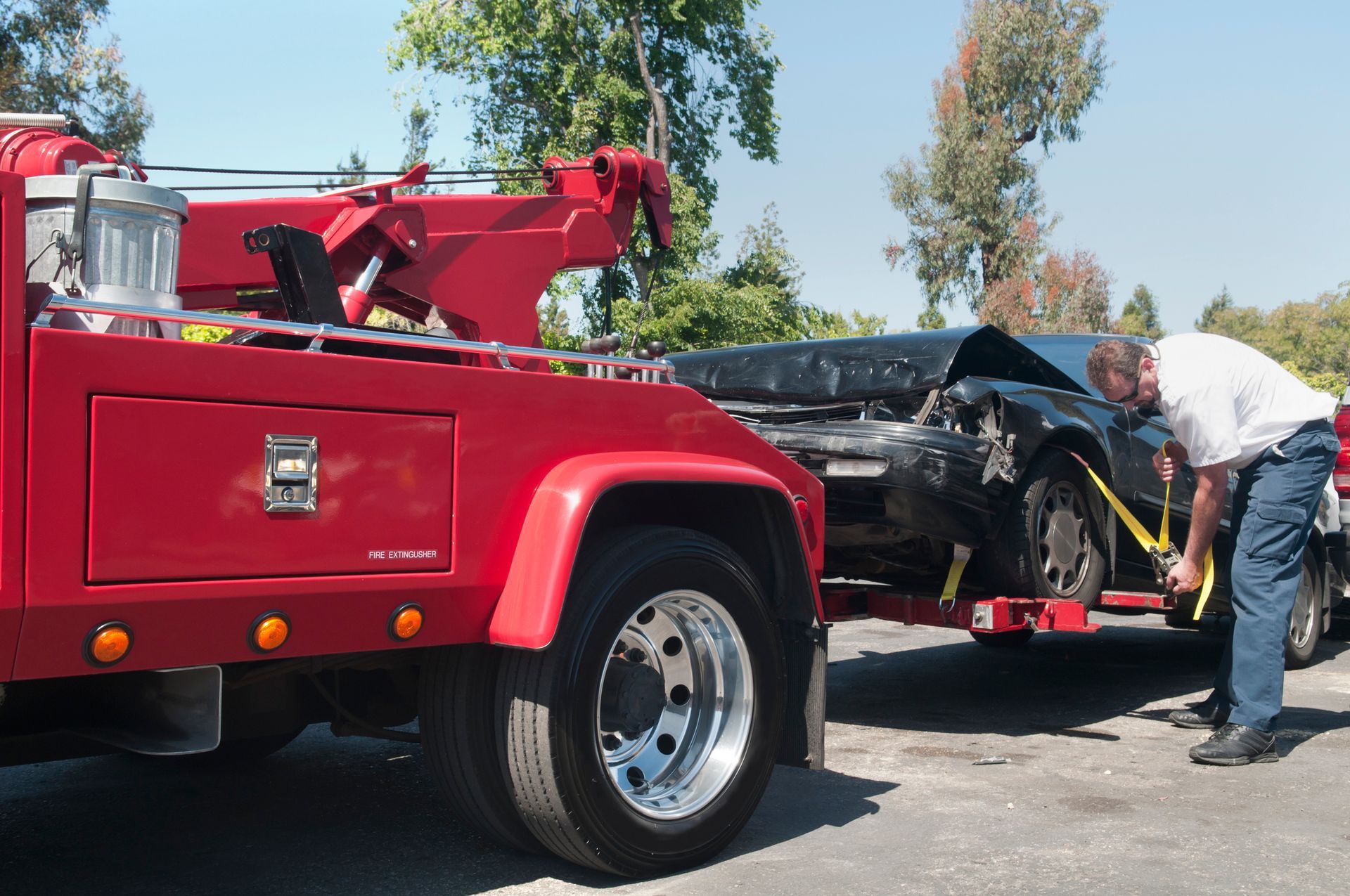 A man is looking under the hood of a car being towed by a tow truck.