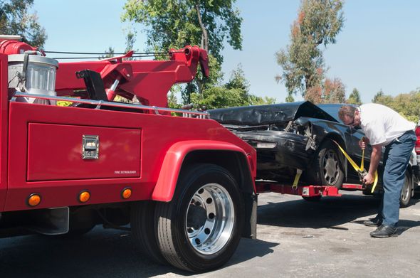A man is looking under the hood of a car being towed by a tow truck.