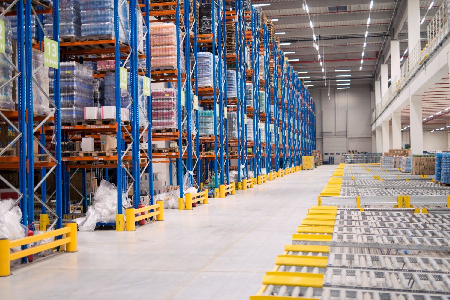 A warehouse interior featuring tall blue metal storage racks filled with inventory, set against a wide concrete floor.