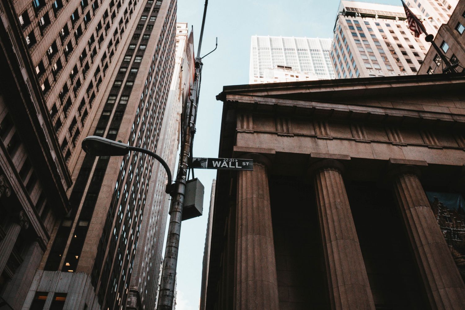 Looking up at the Wall Street street sign and nearby neoclassical architecture in New York City.
