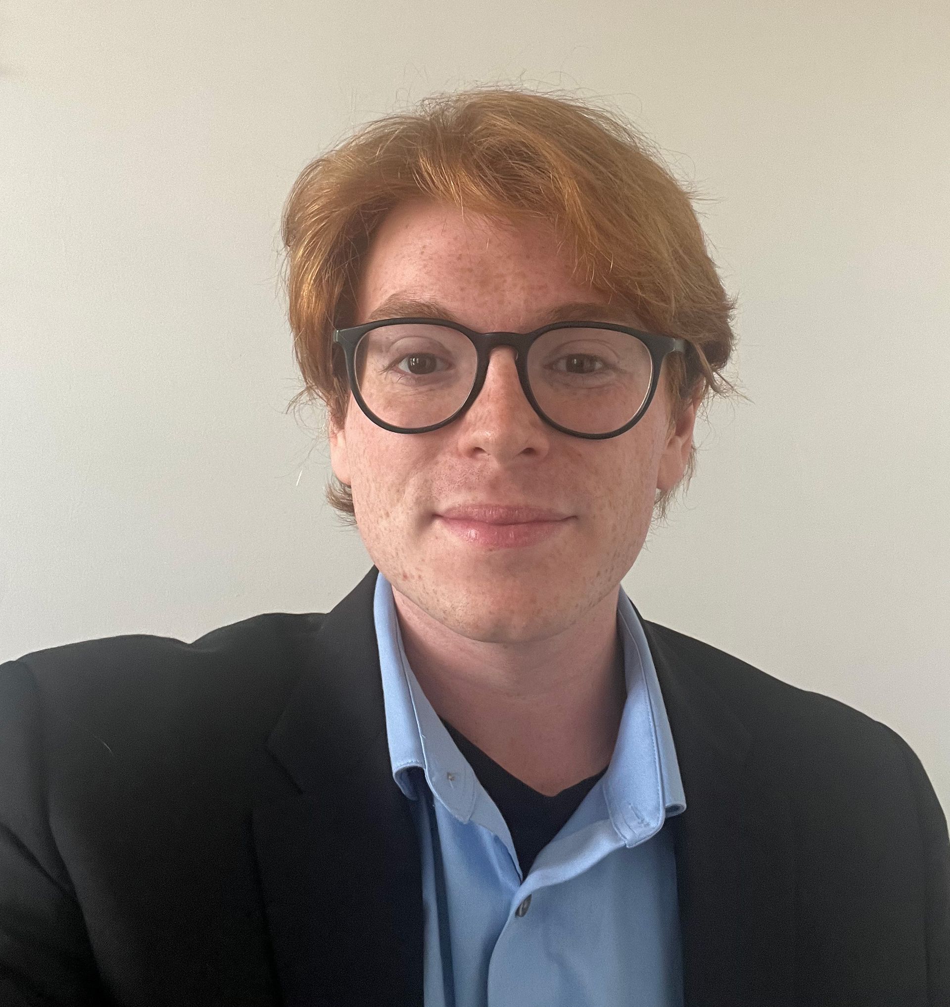 Michael Simon wears a light blue collared shirt and black blazer against a plain white background.