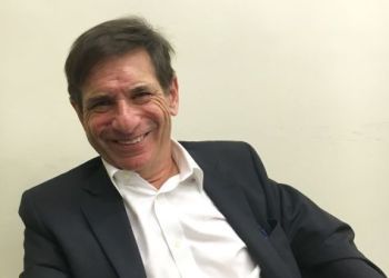 Richard Breier in a dark suit jacket and white collared shirt against a plain, off-white background.