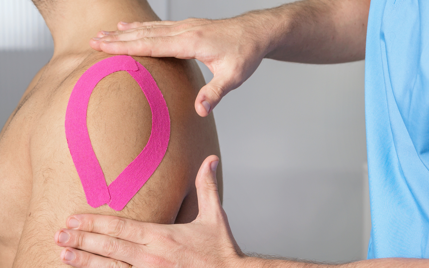 A man is getting a massage with pink kinesio tape on his shoulder.