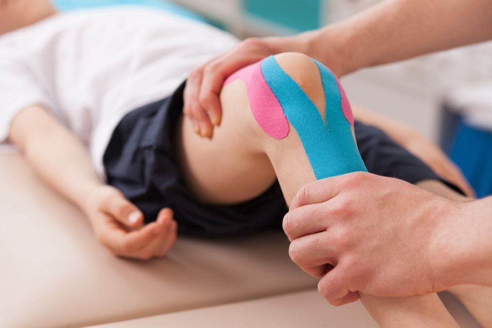 A person is putting kinesio tape on a  knee.