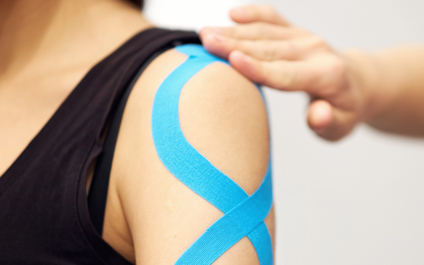 Person's shoulder with blue kinesiology tape, hand on shoulder.