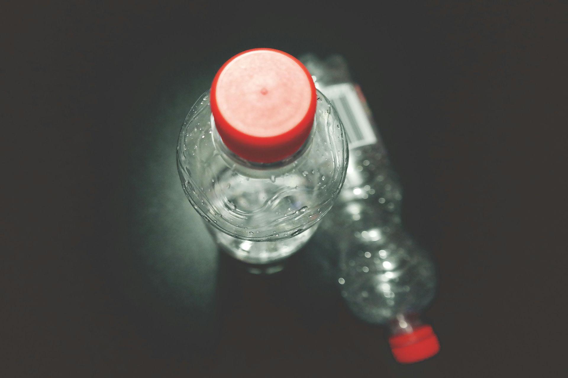 Two clear plastic water bottles with red caps on a dark surface.