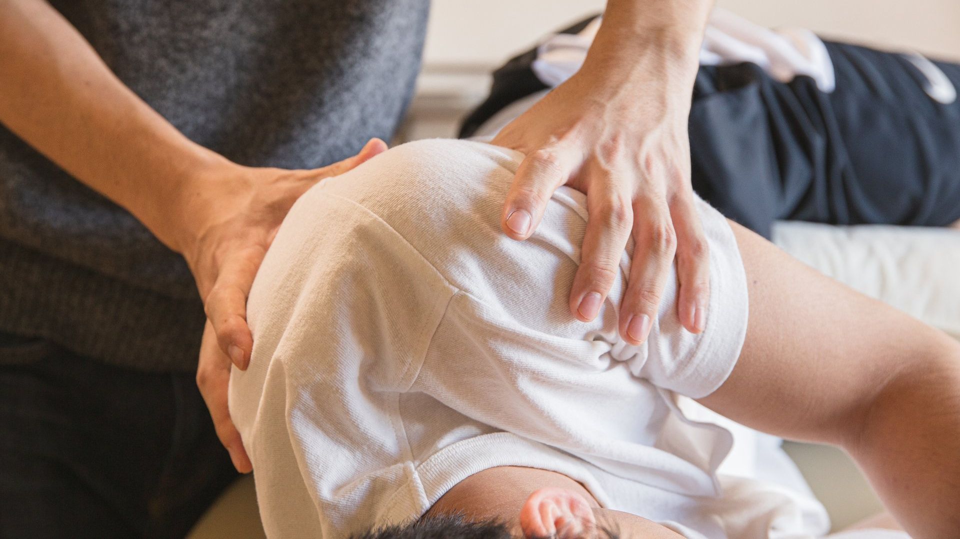 A person is laying on a bed getting a massage by an osteopath.