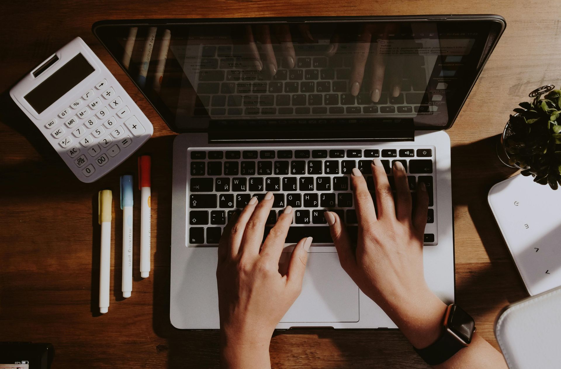 A person is typing on a laptop computer next to a calculator.