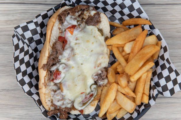 A cheesesteak sandwich and french fries in a basket on a checkered paper
