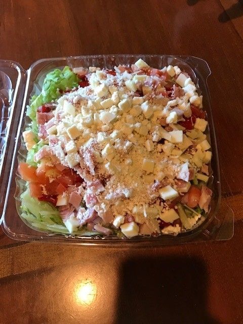 A chef salad in a plastic container on a wooden table