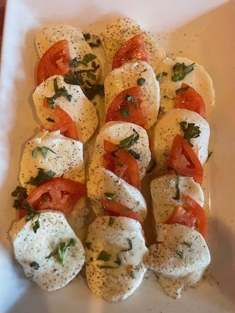 A white plate with mozzarella cheese and tomatoes with black pepper on top