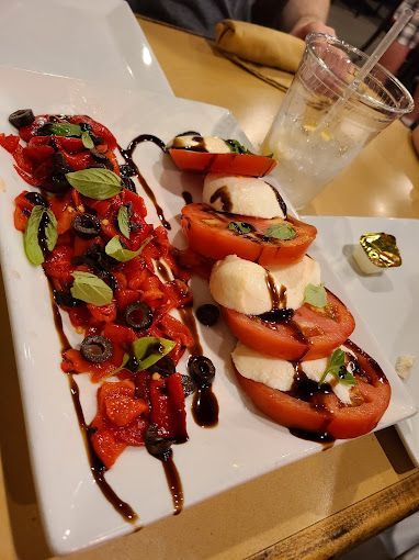 A white plate topped with sliced tomatoes, mozzarella, olives and balsamic glaze