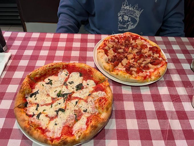 Two personal size pizzas are sitting on a checkered tablecloth on a table