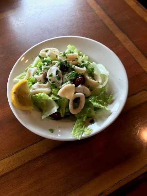 A white plate topped with a seafood salad and a lemon slice on a wooden table.