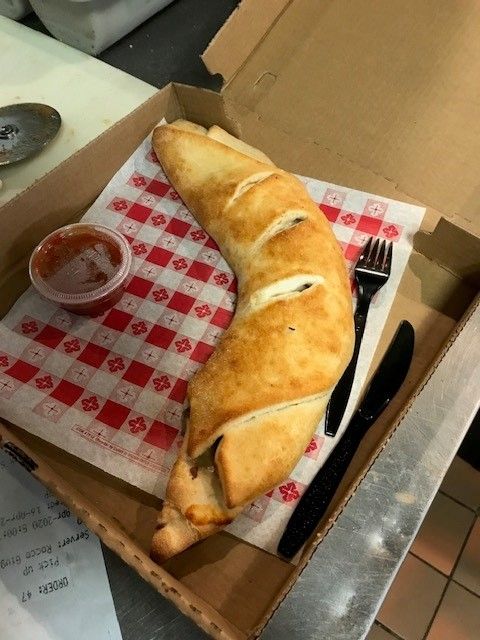A stromboli sitting in a box with a plastic cup of tomato sauce