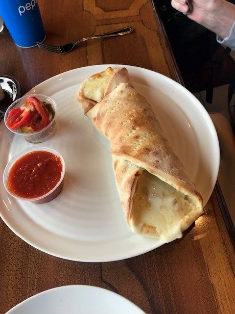 A philly cheesesteak stromboli on a white plate with tomato sauce in a plastic cup