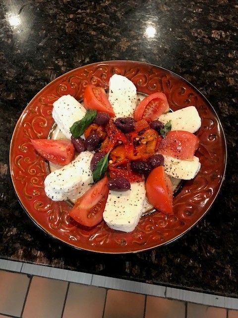 A plate of food with tomatoes, olives, peppers and cheese on a table