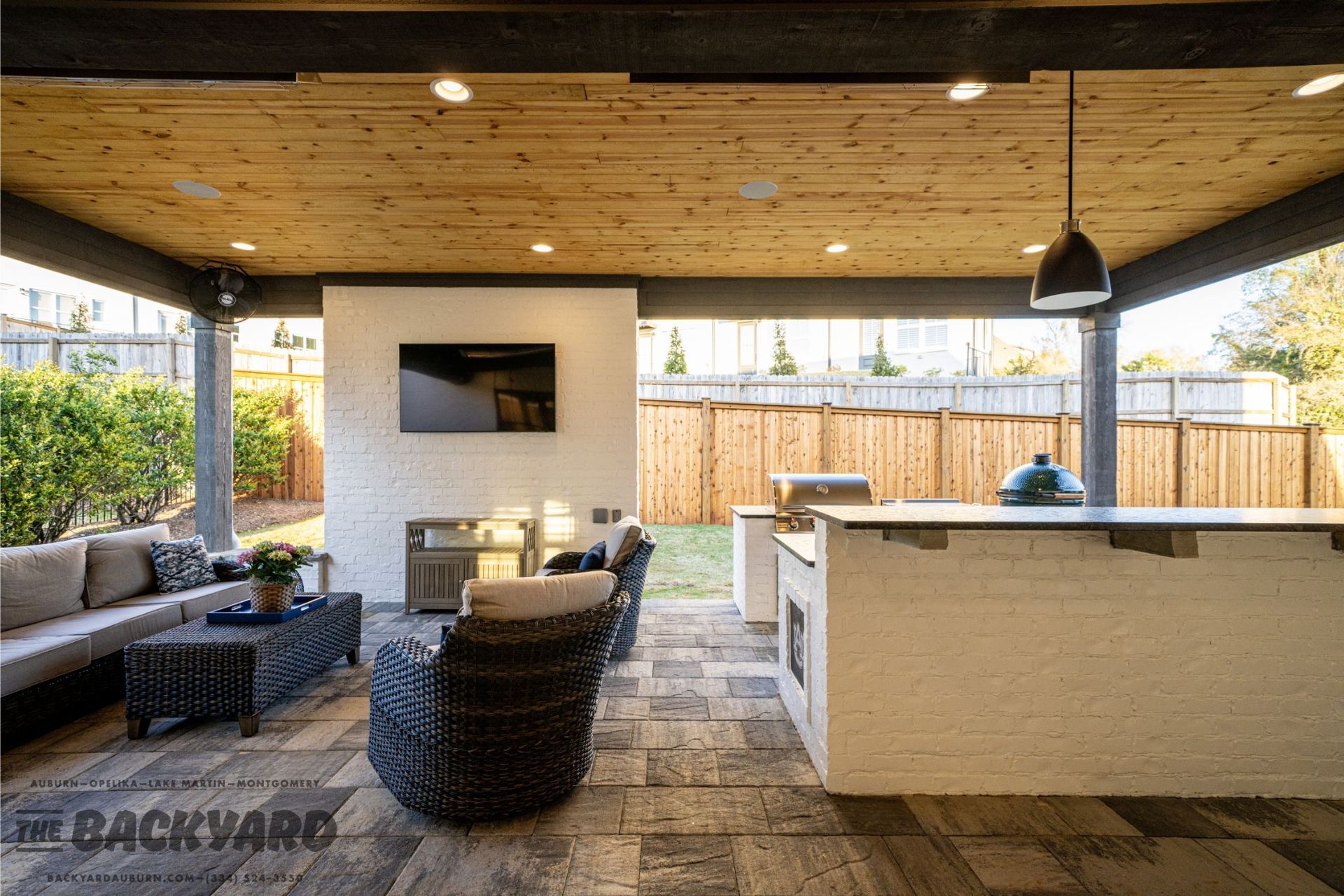 Outdoor living space with seating, fireplace, kitchen, and TV under a wooden ceiling.