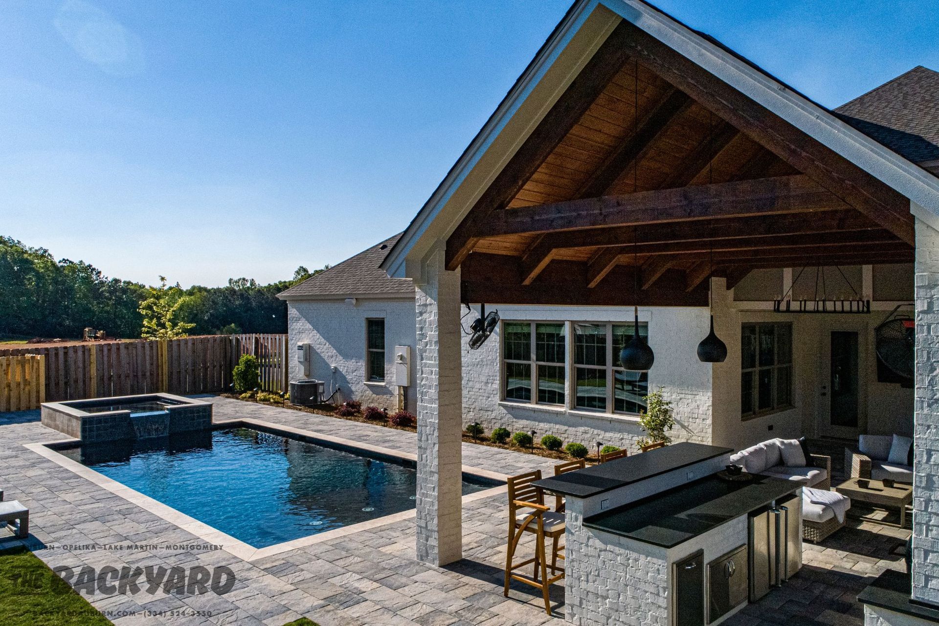 Backyard with pool, covered patio, outdoor kitchen, and seating area; sunny day.